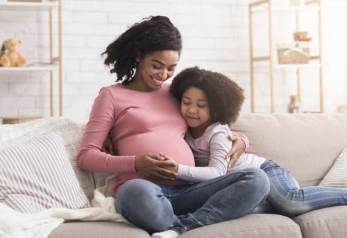 Pregnant woman with daughter sitting on the sofa
